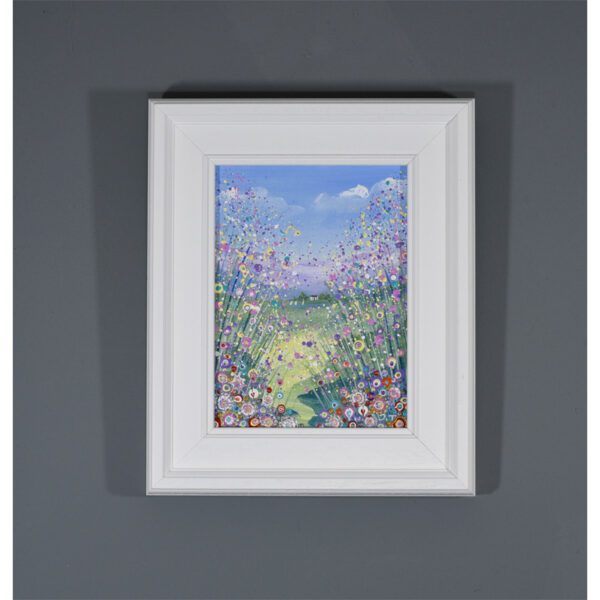 holidays in the sun, an original flower meadow painting by Isle of Wight artist Julia Tanner showing a meadow full of flowers in shades of pink, purple and lemon. The is a pretty cottage and a lake in the distance.