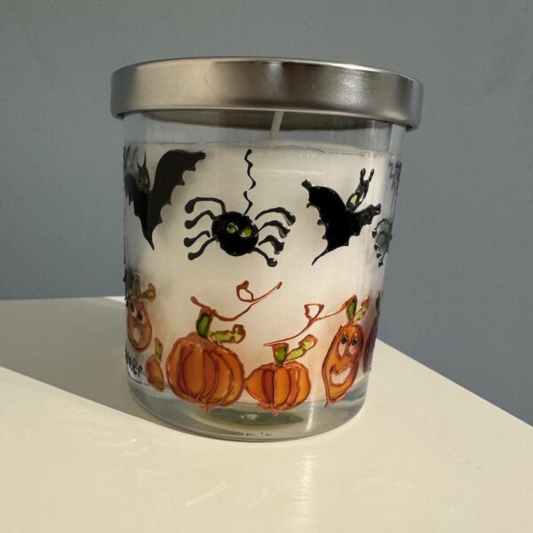 a hand painted halloween candle showing bats, pumpkins, spider and a black cat